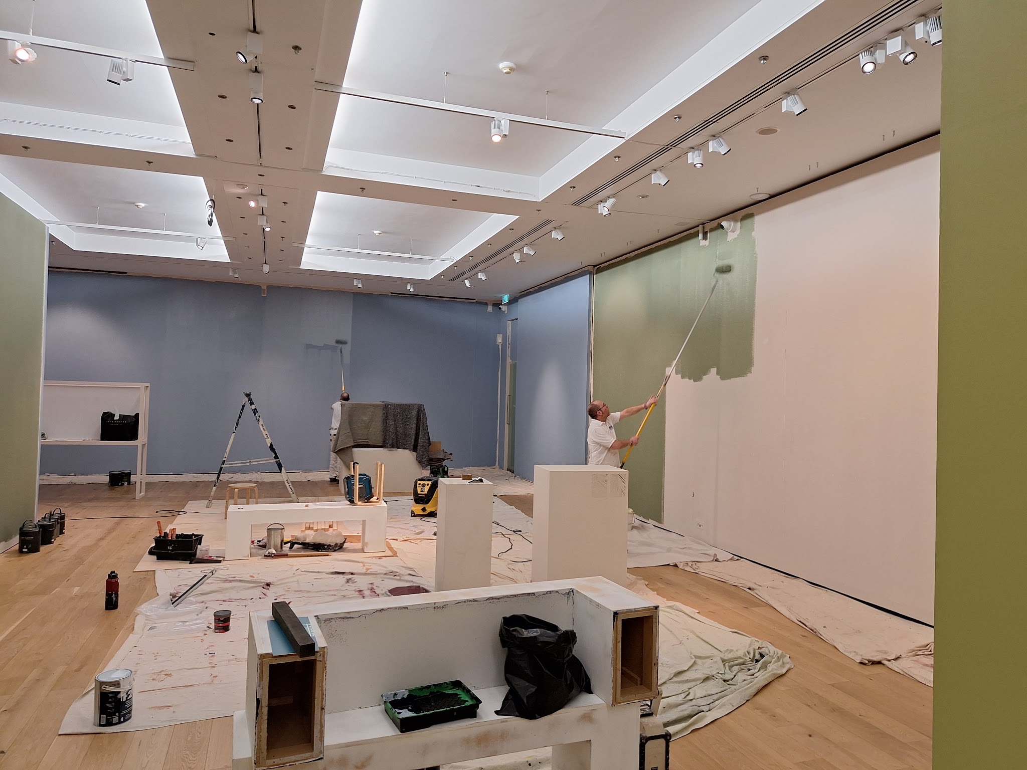 A large commercial interior being painted, with dust sheets down, ladders and a painter on a pole roller