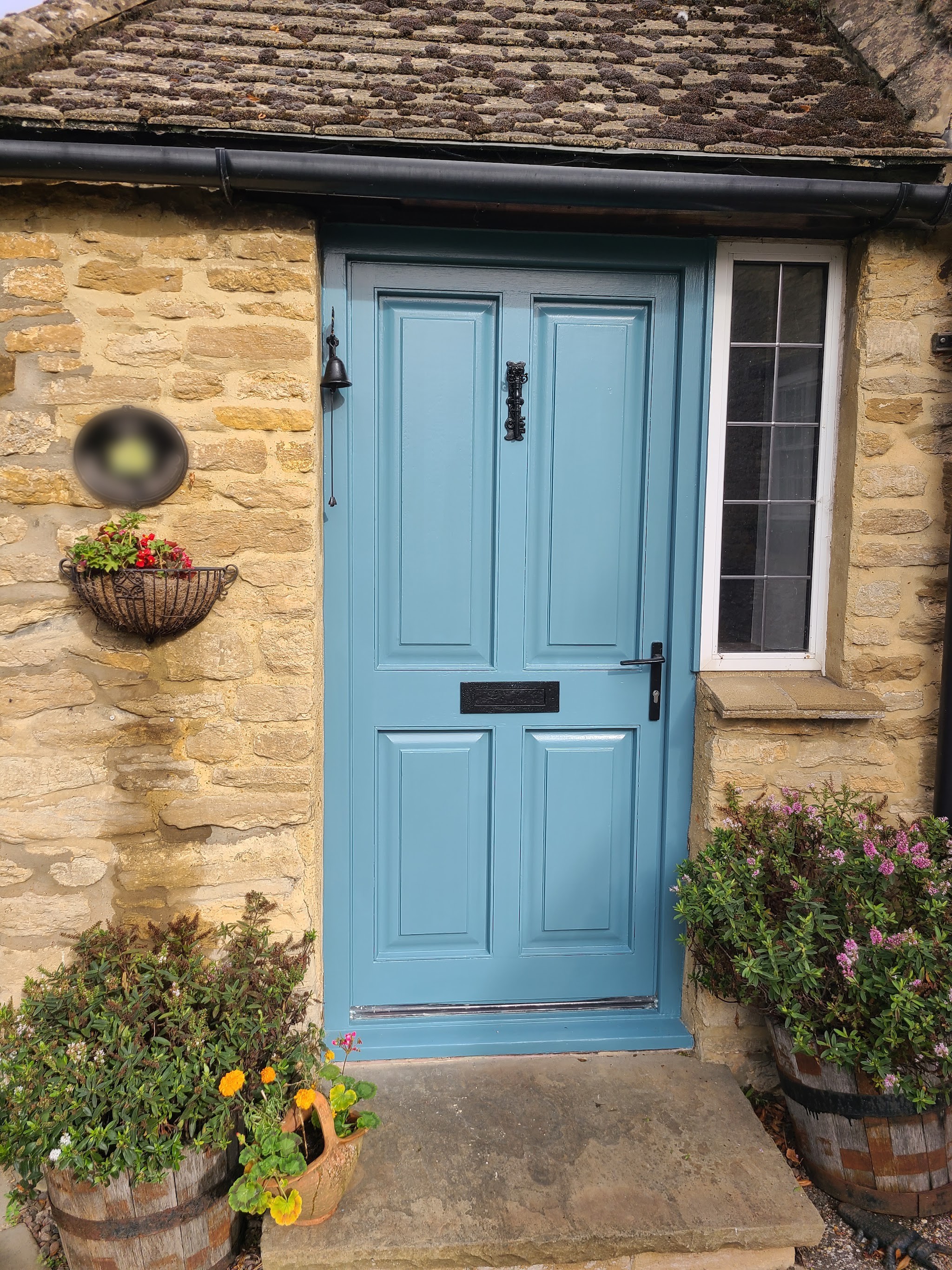 A panelled front door painted soft blue on a stone cottage, with flowers in barrels by the step