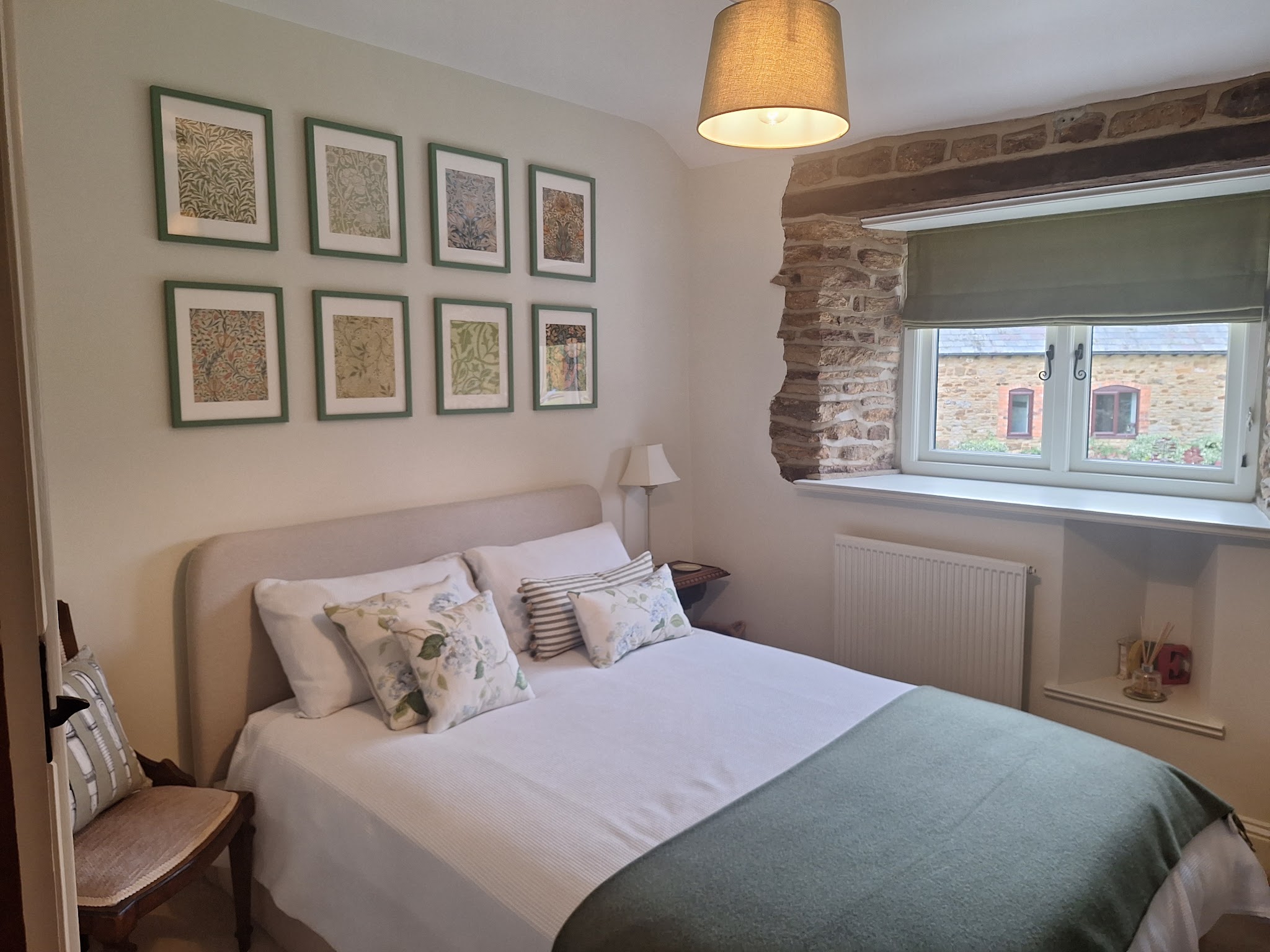 A cottage bedroom decorated in pale tones beside an exposed stone window reveal