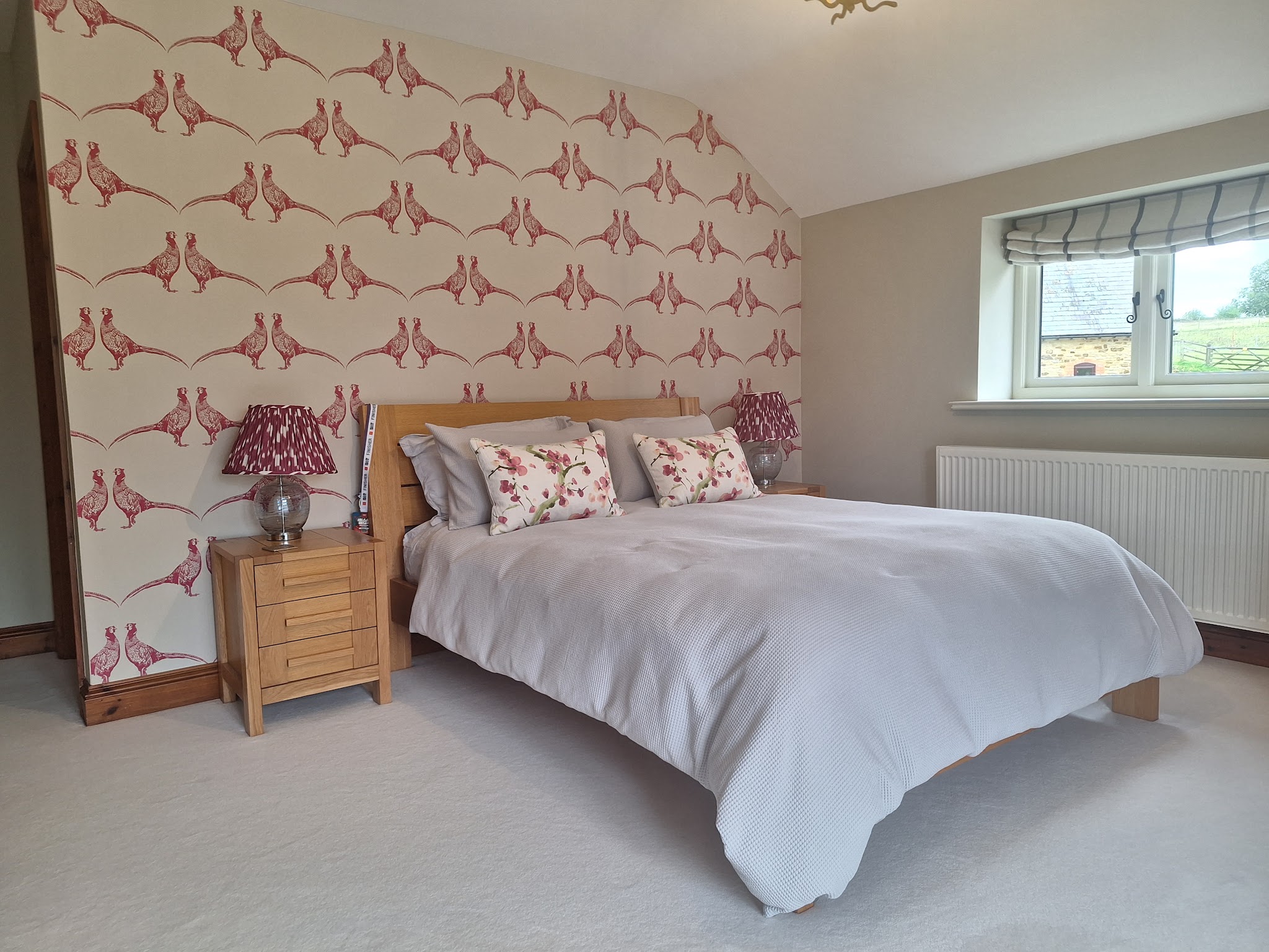 A bedroom with a feature wall hung in a red pheasant-print wallpaper