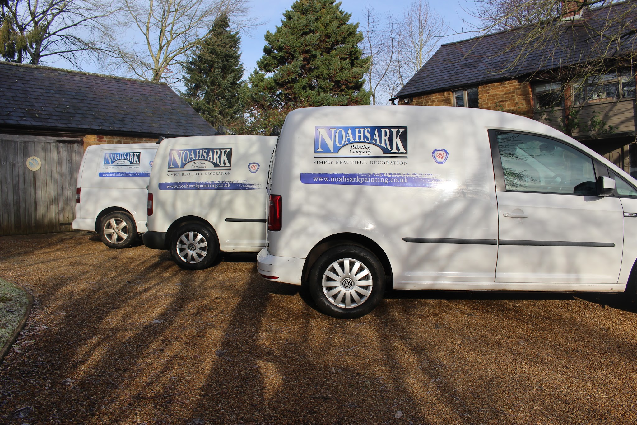 Three white Noah's Ark Painting Company vans lined up on a gravel drive