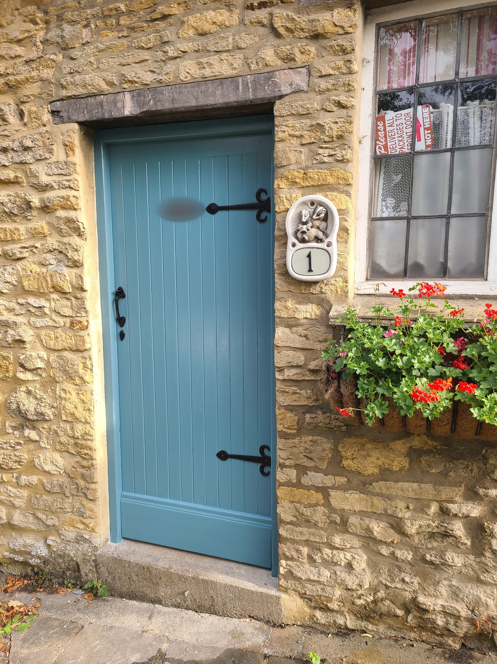 A ledged cottage door painted soft blue, set in Cotswold stone with a window box of geraniums